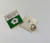A close-up image of the mental health first aider pin badge, showing the pin attachment on the back. The badge is a small square with a white cross symbol and a speech bubble on a green background.