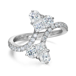 An image of a Rachel Koen women's ring with diamonds, displayed at a slight angle and close-up view. The ring features a white gold band encrusted with small round diamonds leading up to princess cut diamonds set in heart shape at the top in a symmetrical design, each stone held in place by three prongs in white gold. The brilliance of the diamonds is highlighted by the white background, emphasizing the ring's sparkle and intricate setting.