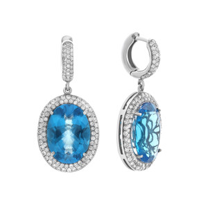 An image of a pair of Rachel Koen women's 14k white gold drop earrings featuring oval-cut blue Topaz surrounded by halos of diamonds. The left earring is shown front-facing, displaying the topaz faceted surface and the sparkling diamonds. The right earring is viewed from a side angle, revealing the depth of the earring and the profile of the blue topaz with a reflective pattern behind it. Both earrings are positioned against a white background and are shown in close-up to highlight the details. The condition of the earrings are pre owned. 