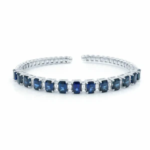 An image of a women's bracelet by Rachel Koen, featuring alternating diamonds and blue sapphires. The bracelet is displayed in a curved, circular position with the open ends facing forward. The angle is slightly elevated, capturing the full row of stones, and the distance allows for a clear view of the intricate design and gemstone details in white gold.
