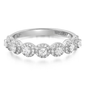 An image of a Messika women's Alliance Joy Demi Tour 18k white gold ring with diamonds, presented in a close-up view with a focus on the top of the band. The ring features a series of large, round-cut diamonds encircled by smaller pavé-set diamonds, creating a continuous sparkling pattern across the front half of the band. The band itself is polished and bears the 'MESSIKA' inscription on one side. The angle of the shot gives a clear view of the intricate setting and the brilliance of the gemstones.