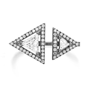 An image of a luxurious Messika women's Toi and Moi ring with diamonds, featuring a unique split-band design on a 18k blackened white gold. The ring is positioned in the center with a front-facing view, showcasing two prominent triangle-shaped diamonds at its open ends, surrounded by a halo of smaller round brilliant-cut diamonds. The intricate setting is visible, and the photograph is taken from a close, direct angle, emphasizing the sparkle and geometric shape of the piece.