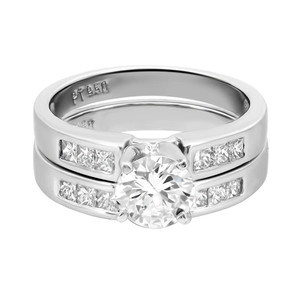 An image of a Rachel Koen brand women's engagement and wedding band ring set with diamonds displayed in a close-up front view. The ring features a prominent central round diamond set in prongs, flanked by two bands encrusted with smaller princess-cut diamonds. The bands are made of a polished platinum with a reflective surface, and the ring is positioned centrally in the frame with a slight tilt, allowing for a clear view of the diamond's facets and the ring's design details. The background is a neutral white, emphasizing the jewelry's brilliance.