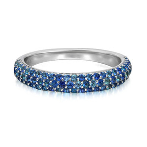 An image of a Rachel Koen women's ring with blue sapphire gemstones, presented in a close-up, frontal view. The ring features a band encrusted with a full circle of round and oval blue sapphire gemstones varying in hue from light to deep sapphire blue, meticulously set to cover the entire visible surface. The band itself is made of polished white gold, with a smooth interior finish, visible on either side of the gemstone-encrusted exterior. The image is taken from a slight angle to showcase the sparkle and varied tones of the blue gemstones.