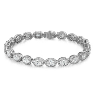 An image of a Rachel Koen brand unisex adult bracelet with diamonds, displayed against a white background. The bracelet is shown in full view, laid out horizontally across the frame, allowing a clear view of its entire length. The design features a series of sparkling oval and round cut diamonds set in a symmetrical pattern, with each diamond encased in a white gold metal setting that connects to the next, forming a continuous line. The diamonds appear to be of various sizes, with some larger stones prominently featured in the middle, surrounded by smaller stones in halo setting enhancing the overall brilliance. The bracelet's clasp is visible at the top center, indicating the bracelet's closure mechanism. The image is taken from a top-down angle at a close distance, ensuring that the intricate details and the shimmer of the diamonds are visible and focused.