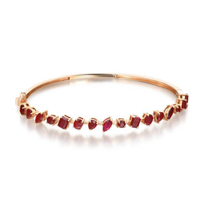 An image of a Rachel Koen women's bangle bracelet with ruby gemstones, presented on a plain white background. The bracelet is positioned horizontally across the center of the frame, with a slight upward curve towards the right side, allowing a clear view of the gemstones. It features a series of red ruby gemstones, set in yellow gold, and each ruby is held by four prongs. The ruby is cut into various alternating shapes: oval, marquise, pear and square, displayed at a medium distance, offering a detailed look at the jewelry's design and craftsmanship.