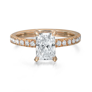 An image of a Rachel Koen brand engagement ring for women, featuring a prominent center radiant cut lab grown diamond in a prong setting. The ring is captured in a close-up frontal view on a white background, showcasing the diamond's facets and brilliance. The yellow gold band is encrusted with smaller round-cut diamonds halfway around, providing a continuous sparkle. The angle of the photo emphasizes the ring's profile and the alignment of the band's diamonds.