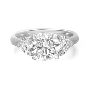 An image of a Rachel Koen women's engagement ring with lab grown diamonds, showcasing a front view with a slight angle to emphasize the central large round-cut diamond flanked by two smaller round-cut diamonds, all set in a polished white gold band. The ring is captured up-close against a white background, highlighting its brilliance and design details.