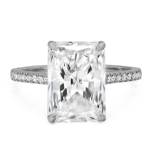 An image of a Rachel Koen brand women's engagement ring with lab grown diamonds, showcasing a prominent rectangular-cut diamond in a four-prong setting at the center. The ring is pictured from a front-facing angle with a close-up view, emphasizing the central stone's sparkle and the encrusted smaller diamonds along the band's upper half. The white gold metal band displays a polished finish, complementing the brilliance of the diamonds. The background is neutral, highlighting the ring's details.