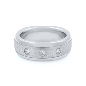 An image of a unisex adult wedding ring by Rachel Koen, featuring a brushed 14k white gold band with a bright polish at the edges. Three round-cut diamonds are equidistantly set across the center, catching the light. The ring is photographed at a slight angle, highlighting the shimmering diamonds and the contrast between the brushed and polished surfaces. The image is a close-up, providing a clear view of the ring's texture and design.