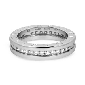 An image of a Bvlgari B.Zero1 unisex adult ring with diamonds, displayed in a close-up side view on a white background. The ring is centered and shown at a slight angle, allowing both the outer band with inscriptions and the inner band encrusted with diamonds to be visible. The diamonds are set in a single row, and the white gold parts of the ring reflect light, indicating a polished finish.