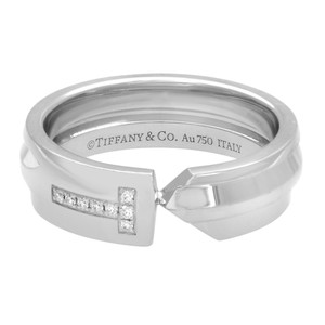 An image of a women's Tiffany & Co. T ring with diamonds, displayed in a close-up side view. The ring features a thick 18k white gold band with a T design set with multiple small round diamonds. The Tiffany & Co. logo and purity mark "Au750 ITALY" are engraved inside the band. The ring is photographed against a white background, with the focus on the diamonds and brand engraving. The ring is pre owned in great condition. 