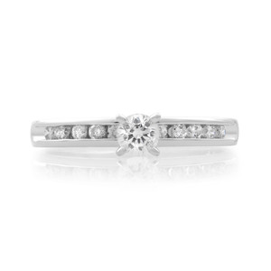 An image of a Rachel Koen women's engagement ring with diamonds, showcasing a central round-cut diamond in a prong setting, flanked by a row of smaller channel-set diamonds on a polished platinum band. The ring is photographed head-on at a close distance, providing a clear view of the sparkle and design.