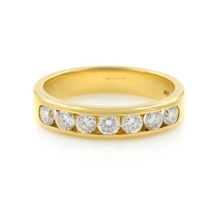 An image of a Rachel Koen women's wedding band ring with diamonds. The ring is presented in a close-up, front-facing view against a white background. It features a polished 18k yellow gold band with a row of round-cut diamonds set in a channel setting across the top half. The diamonds are evenly spaced and catch the light, indicating their clarity and cut. The band appears to be of a medium thickness with a slightly curved outer edge, and the inside of the band shows a hallmark visible at this angle. The camera's focus is sharp, highlighting the details of the diamonds and the golden hue of the band.