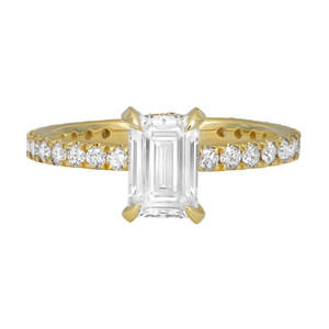 An image of a Rachel Koen brand women's engagement ring with lab grown diamonds. The ring is presented in a close-up, front view showcasing a prominent emerald-cut center diamond. It is prong-set and elevated above a yellow gold band, which is encrusted with smaller round-cut diamonds in prong setting along its circumference. The angle of the photograph allows for a clear view of both the ring's band and the facets of the central diamond.