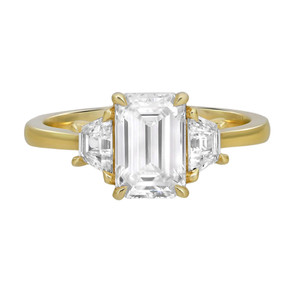 An image of a Rachel Koen women's engagement ring with lab grown diamonds, centered and shown at a close front angle against a white background. The ring features a prominent rectangular emerald cut centre diamond, flanked by smaller trapezoid diamonds on both sides, all set on a polished yellow gold band.