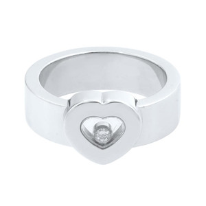 An image of a Chopard Happy Diamond women's ring, displayed in a front-facing position. The ring features a thick, polished white gold band with a heart-shaped setting at the top center, holding a single sparkling diamond. The angle of the photograph provides a clear view of the heart detailing and the diamond's placement within it, with the ring appearing to be at a close distance for detailed inspection. The background is uniformly white, emphasizing the ring's design and shine.The ring is pre-owned in a great condition.