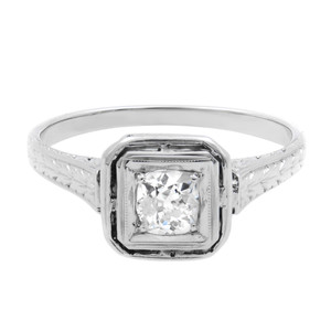 An image of a Rachel Koen women's antique engagement ring with diamonds, featuring a prominent round-cut diamond center stone in a bezel setting, positioned front and center. The ring is viewed from a top angle, showcasing the detailed engravings along the platinum band, which is angled slightly to the right, offering a clear view of the ring's profile. The image is taken from a close, yet comfortable distance that highlights the ring's design and the reflective facets of the diamonds. The ring is pre-owned in a good condition. 