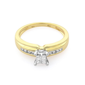 An image of a Rachel Koen women's engagement ring with diamonds, displayed in a close-up front view. The ring features a polished 14K yellow gold band with a row of channel-set round diamonds on each side leading up to a prominent square center stone held by prongs. The ring is positioned against a white background, with the band angled slightly to the left, giving a clear view of the diamonds' facets and the band's interior engraving. The image is taken from a medium distance, showcasing the ring's details and design. The ring is pre-owned in a great condition.