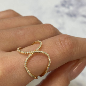 An image of a women's Rachel Koen brand fashion ring with diamonds, showcased on a finger at a close-up angle. The ring features a unique open design with two intertwined yellow gold bands encrusted with small, sparkling diamonds. The photo is taken from a top-down perspective, focusing on the top and side of the ring, with a soft, blurred background that accentuates the ring's detail and brilliance.