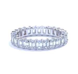 An image of a Rachel Koen women's eternity platinum ring with diamonds, showcased centrally against a white background. The ring is positioned horizontally with the focus on the top side displaying a full circle of emerald-cut diamonds in a channel setting. The diamonds are evenly spaced and secured by shared prongs, offering a continuous sparkle. The angle is a near eye-level view, and the distance is close-up, providing a clear view of the diamond's facets and the ring's intricate design.