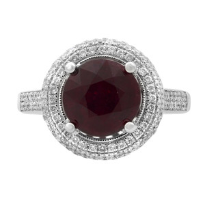 An image of a Rachel Koen women's engagement ring with ruby and diamonds, displayed in top view. It features a central, large, round-cut red ruby surrounded by two concentric circles of smaller sparkling diamonds set in a white gold band, which is also encrusted with diamonds on its top surface. The ring is positioned centrally against a white background, with the band horizontally aligned and the gemstone facing directly upwards, providing a clear and detailed view of the ring's design and craftsmanship.
