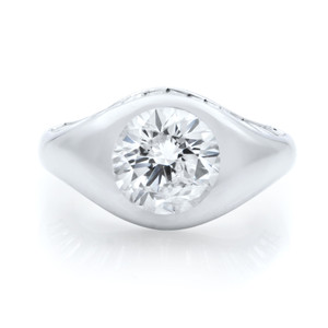 An image of a Rachel Koen women's ring with diamonds prominently displayed in a front-facing view. The ring features a large, central round-cut diamond set in a smooth, polished platinum band that twists around the stone. The band's surface curves up to cradle the diamond, which is positioned centrally and catches the light from various angles, highlighting its clarity and brilliance. The ring is photographed at a close distance against a white background, with a slight shadow beneath it indicating its placement on a reflective surface.