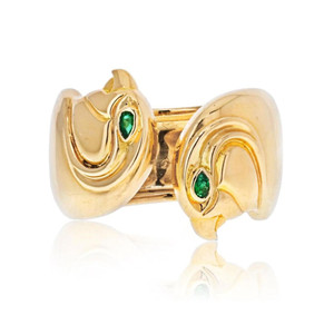 An image of a Vintage Cartier Anoubois women's ring with gemstones, showcased on a reflective surface. The ring is captured at a close distance and centered in the frame, with a front-facing angle that highlights its design features. The ring has a polished yellow gold band with a distinctive, abstract, sculptural form. Two bright green gemstones are set within yellow gold, one on each side, adding a touch of color and elegance to the piece. The reflection of the ring is visible beneath it, creating a symmetrical effect. Comes in a great preowned condition.