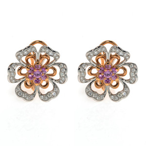 An image of a pair of new Luca Carati women's earrings featuring a floral design, viewed from the front at a medium distance. The earrings have rose gold and white gold petals accented with small round diamonds and central pink sapphire gemstones in a purple hue. The intricate details and sparkle of the diamonds are clearly visible.