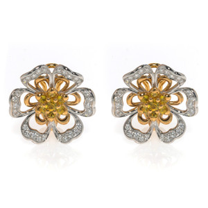 An image of a pair of Luca Carati women's earrings, featuring a symmetrical floral design with diamonds and yellow sapphire gemstones. The earrings are positioned side by side, facing forward, with a medium-close perspective. The petals are outlined with a pavé of round diamonds, while the center showcases a cluster of yellow sapphire gemstones, all set in white gold and rose gold. The background is white, highlighting the intricate details and luxurious appearance of the jewelry.