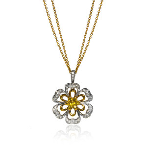 An image of a new Luca Carati women's necklace with diamonds and yellow sapphires, featuring a pendant in the shape of a flower with yellow and white gold, and encrusted with multiple sparkling diamonds. The pendant is centrally positioned at a direct front angle, hanging from a gold chain with a slight reflection visible below, indicating the pendant's proximity to a reflective surface. The photo is taken from a close distance, highlighting the intricate details of the diamonds and design.