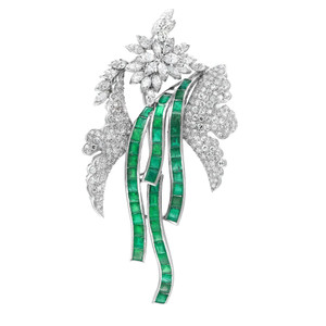 An image of a luxurious Rachel Koen estate vintage brooch featuring a floral and ribbon design, adorned with sparkling diamonds and rich emerald gemstones. The brooch is captured in a close-up view against a white background, displaying the intricate details and craftsmanship. The diamonds create a dazzling contrast with the vibrant emerald gemstones, which are arranged in a flowing ribbon-like pattern set in a platinum. The piece is angled to show the three-dimensional quality of the gemstone settings and the overall dynamic design. The brooch is pre owned in a great condition. 
