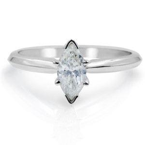 An image of a Rachel Koen brand women's engagement ring with diamond, featuring a close-up front view. The ring is centered with the focus on a marquise-cut solitaire diamond set in a north-south orientation on a polished white band. The angle of the shot and the lighting create a reflection of the ring on the surface below it, suggesting the ring is placed on a reflective surface at a slight distance, emphasizing the diamond's sparkle and the band's shine.