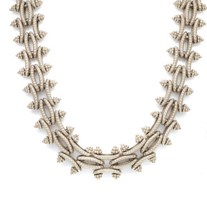 An image of a Stephen Dweck brand unisex adult 18k yellow gold necklace without stones, displayed against a white background. The necklace features a series of intricate, interlocking metal segments with a textured finish, creating a vine-like pattern. The design includes small, bead-like details clustered at intervals along the metalwork, which adds dimension and visual interest. The necklace is positioned in a gentle curve with the focal point centered and the ends flowing outwards towards the top corners of the image, suggesting its natural drape when worn. The photo is taken from a top-down perspective, providing a clear and detailed view of the necklace's craftsmanship.