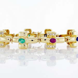 An image of a luxurious Catherine Mullen women's bracelet with diamonds and gemstones. The bracelet is positioned horizontally across the center of the frame, viewed from a close distance, and captured at eye level. It features a series of gold links, each adorned with a central emerald, ruby and sapphire and flanked by smaller diamonds. The polished yellow gold links and sparkling gemstones are crisply focused, casting reflections on the white surface below. Bracelet is in excellent preowned condition.