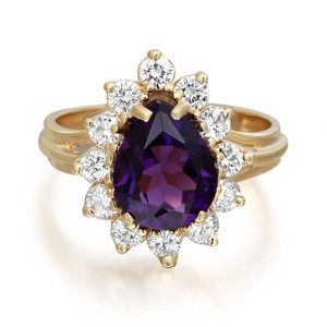 An image of a Rachel Koen women's ring, viewed from a top-down angle, showcasing a prominent oval-cut amethyst in a deep purple hue, set in the center. The central stone is framed by a sparkling halo of round-cut diamonds, all mounted on an elegant yellow gold band. The ring is captured up close, filling the frame, and is well-lit, emphasizing the luster of the gemstones and gold.