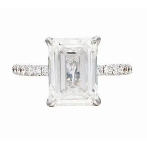 An image of a Rachel Koen brand women's engagement ring with diamonds. The ring is displayed front and center with a close-up view, showcasing a prominent emerald-cut center diamond in a prong setting in white gold. The band is adorned with smaller round-cut diamonds, extending halfway down its length. The image captures the ring at a straight-on angle against a neutral background, highlighting the sparkle and clarity of the diamonds.