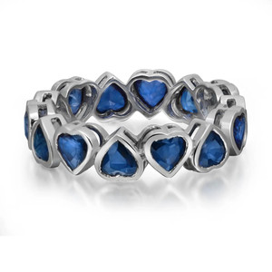 An image of a women's Rachel Koen ring adorned with heart-shaped blue sapphire gemstones in white gold. The ring is positioned at a slight angle, showcasing its intricate design from a close-up perspective. The gemstones are set in a continuous band, and the image captures the ring at eye level, highlighting its elegant and detailed craftsmanship.