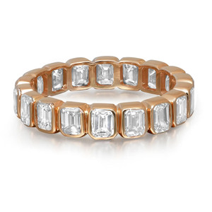 An image of a women's ring with diamonds by Rachel Koen. The ring is displayed at a front angle, showcasing its continuous band of emerald cut diamonds set in yellow gold bezel setting. The photograph is taken at a close distance, highlighting the clarity and arrangement of the diamonds around the band.