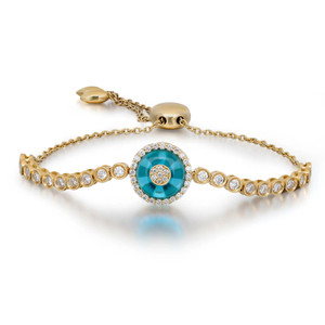 An image of a bracelet designed by Rachel Koen, featuring a central round blue glass surrounded by diamonds. The bracelet is displayed at a slight angle, emphasizing its intricate detailing in yellow gold. It is positioned at eye level and photographed at a close distance to highlight the elegance of the diamonds along the band. The unisex design showcases a chain with an adjustable clasp in the background.