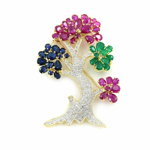 An image of a brooch designed like a stylized tree, adorned with diamonds and ruby, emerald, sapphire viewed from a slightly elevated angle. The brooch features a diamond-encrusted trunk with branches extending to clusters of vibrant ruby, emerald, sapphire gemstones, resembling flowers. The image is taken at a close distance, highlighting the intricate details and vibrant colors of the piece, set against a plain white background.Excellent pre-owned condition. 