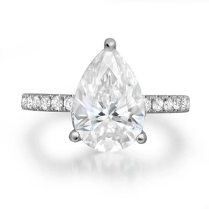 An image of an engagement ring with diamonds, designed for women by Rachel Koen. The ring features a large pear-shaped diamond at the center, with smaller round diamonds adorning the white gold band. The ring is positioned upright, facing directly towards the viewer. The photo is taken from a close distance, highlighting the intricate details and sparkle of the diamonds against a plain white background.