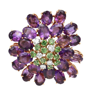 An image of a Rachel Koen unisex adult brooch featuring a circular arrangement of gemstones. At the center, sparkling white diamonds are surrounded by vibrant green quartz gemstones. Radiating outward, a layer of deep purple amethyst  gemstones completes the design in yellow gold. The brooch is shown from a top-down angle, centrally positioned and captured at a close distance to highlight the intricate detailing and color contrasts. Great preowned condition.