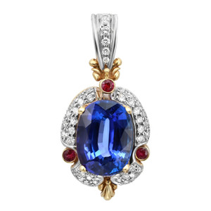 An image of a women's pendant by Rachel Koen, featuring a central large blue tanzanite gemstone encircled by sparkling diamonds. Red ruby gemstones are strategically positioned around the central stone in white and yellow gold. The pendant is shown from the front, captured from a close-up angle to highlight its intricate details and craftsmanship. No chain included. Great preowned condition.