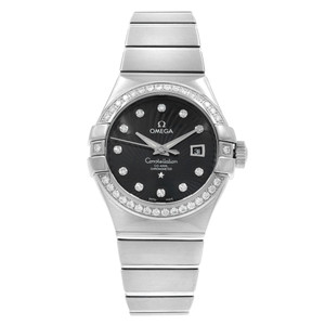 An image of an OMEGA Constellation women's wristwatch displayed from a front-facing angle at a close distance. The watch features an 18k white gold band and a black dial with diamond hour markers. It includes a date indicator and luminous hands, and the bezel is adorned with diamonds. The overall condition appears to be a display model.