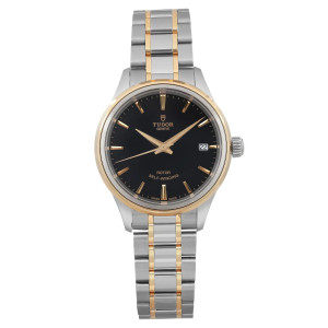 An image of a TUDOR Style 34mm women's wristwatch, displayed from a front-facing angle at a close distance. The watch features a black dial with yellow gold hour markers and hands, along with a date indicator at the 3 o'clock position. The bezel is gold, complementing the two-tone steel and gold bracelet. The watch is in unworn condition.