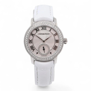 An image of a pre-owned Audemars Piguet Jules Diamond 18K White Gold Diamond Silver Dial Women's Watch 77228BC. The watch is positioned upright, facing directly towards the viewer, showcasing its round dial with Roman numerals and a small sub dial. The bezel is adorned with sparkling stones, and the watch is paired with a white leather strap. The photo is taken from a close-up angle, capturing the intricate details of the watch's face and strap.