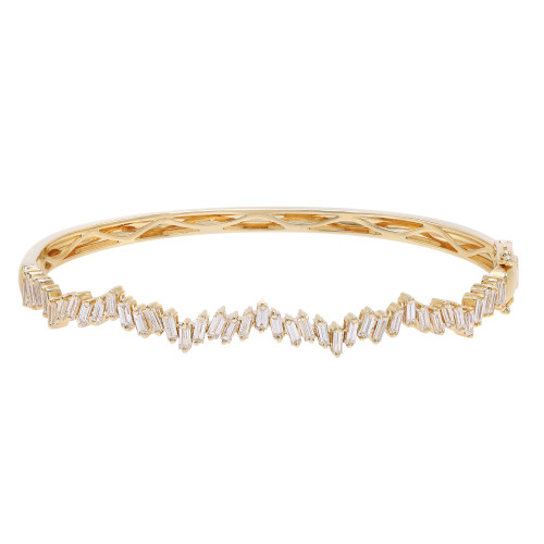 An image of a Rachel Koen women's bracelet with diamonds displayed horizontally against a white background. The bracelet is in sharp focus, showcasing a series of shimmering, baguette-cut diamonds arranged in a zigzag pattern along the top half. The yellow gold band of the bracelet has a smooth, polished finish with geometric cut-out designs visible on the underside. The view is from a top-down perspective, capturing the jewelry piece from a close, but ample distance to appreciate its full design and luxurious appearance.