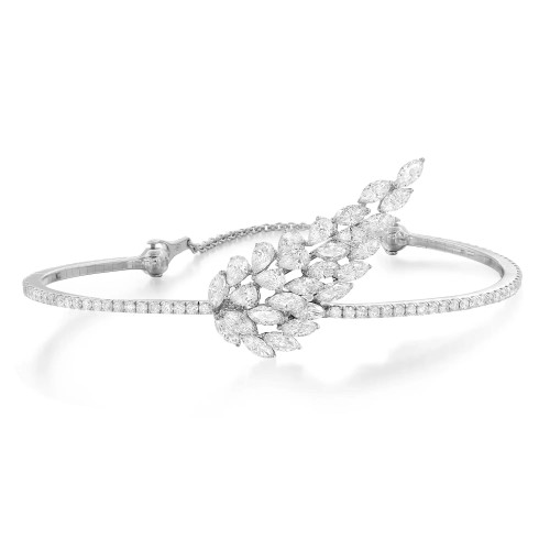 An image of a Messika women's Angel Skinny 18k white gold diamond bangle bracelet, presented on a plain background. The bracelet is positioned in a slight curve, with the left side closer to the viewer and the right side extending away at a gentle angle. The focal point features a cluster of marquise-cut diamonds arranged in a feather-like pattern, creating a dynamic sense of movement. The diamonds sparkle against the metal setting, and the bracelet band is encrusted with smaller, round-cut diamonds that catch the light. The piece is photographed from a front-facing angle at a close distance, allowing for detailed appreciation of the diamonds' cuts and the bracelet's intricate design.