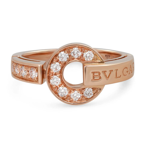 An image of a Bvlgari Bvlgari women's ring with diamonds, showcased in a close-up view on a plain background. The ring is angled to display the top and side, highlighting the circular design with embedded diamonds and the brand name "BVLGARI" engraved on the band. The rose gold metal contrasts with the brilliance of the diamonds. The image is taken from a slightly elevated angle, providing a clear view of the ring's details. The condition of the ring is new. 
